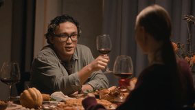 Medium shot of diverse young couple toasting with wine glasses while sitting at festive table during Thanksgiving celebration at home - Powered by Shutterstock - Get 15% off with code: PIKWIZARD15