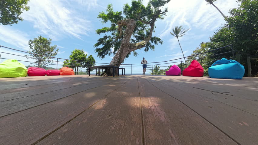 Woman Standing at the Edge of a Deck Gazing Over Jungle Landscape and Distant Sea Under a Bright Sky, Wide Angle, Peaceful Moment Concept.
