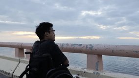a person in a wheelchair gazes at a serene seascape, bathed in the soft hues of the horizon. The image evokes a sense of introspection and peace disability asian man - Powered by Shutterstock - Get 15% off with code: PIKWIZARD15