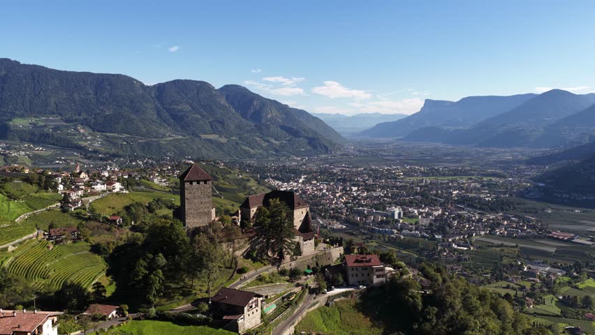 Tyrol Castle, surrounded by apple orchards and mountains, in summer time. Aerial daytime drone video.
