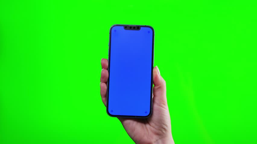 Hands holding smartphone with blue screen on green background.