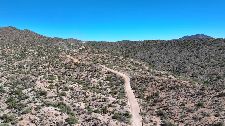 Aerial view of off-road Raptor trucks racing along 17 Mile Road near Wikieup, Arizona, showcasing a winding dirt road and sparse desert vegetation, Wikieup, Arizona, United States.
