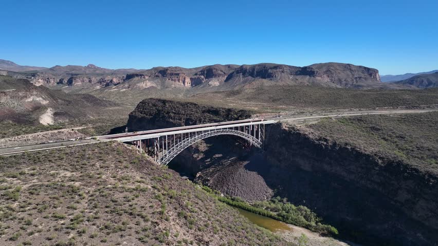 Aerial view of the Burro creek bridge spanning a rocky canyon with sparse vegetation, under a clear blue sky, Wikieup, Arizona, United States.