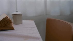 A person pulls out a brown leather chair to sit at a table. An open book rests on the white tablecloth. Minimalist bright interior. - Powered by Shutterstock - Get 15% off with code: PIKWIZARD15