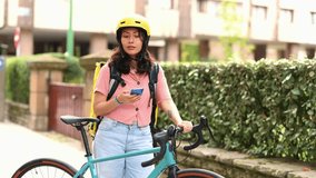 Young female courier with a thermal backpack using her phone to find the delivery address in the city, standing next to her bicycle while working for a food delivery service on a sunny day - Powered by Shutterstock - Get 15% off with code: PIKWIZARD15