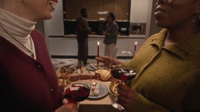 Focus on two diverse women chatting and drinking red wine while boyfriends standing in background during Thanksgiving celebration at home - Powered by Shutterstock - Get 15% off with code: PIKWIZARD15