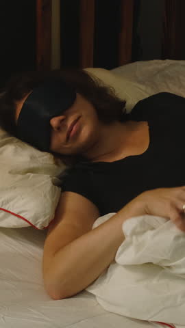Vertical video. Woman in sleep mask lying in bed preparing for healthy and deep sleep
