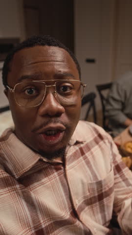 Vertical POV shot of young African American man vlogging on camera while dining with multiethnic friends on Thanksgiving Day