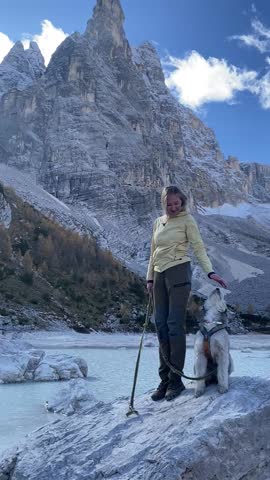 Woman with dog standing on rock by turquoise mountain lake Sorapis in Dolomites Italy