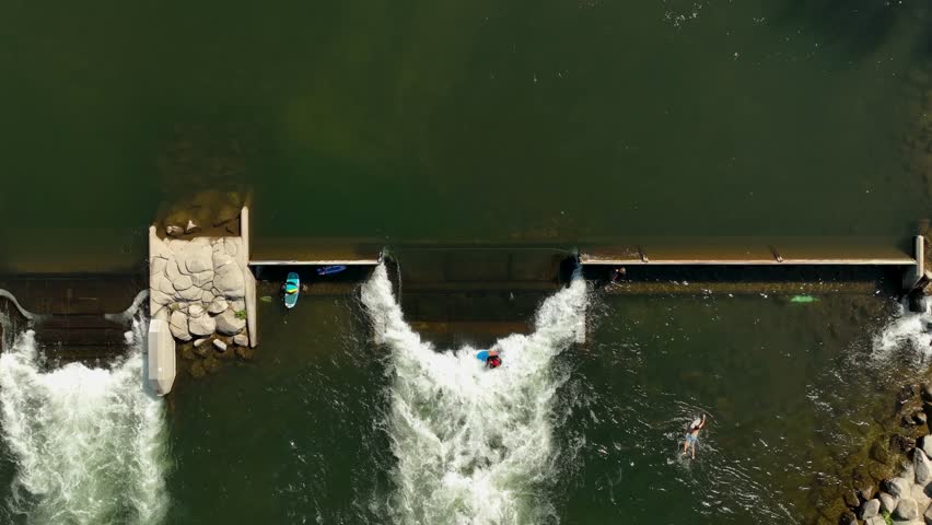 Overhead aerial of reservoir spillway with kayaker paddling in whitewater rapids