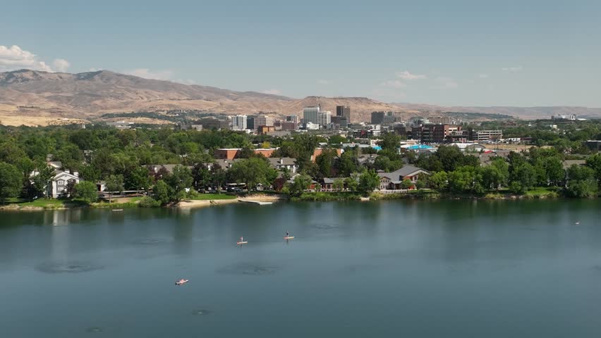 Aerial of Boise, Idaho skyline over a tranquil river with people paddleboarding.
