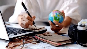 A person is planning a trip with a globe, laptop, camera, notebook and pen on a table. Accessories include passport and sunglasses for a great travel experience. - Powered by Shutterstock - Get 15% off with code: PIKWIZARD15