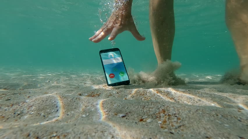 Woman drops smartphone into water while standing in sea, mobile phone falls onto sandy seabed, female hand picks up cellphone