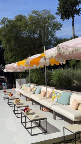 Close-up of a chic poolside chill zone with umbrellas, soft sofas, bright lemon-themed cushions, and outdoor tables, capturing a vintage Italian Dolce Vita summer vibe