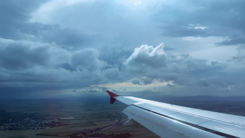 plane flying high above dark thunderstorm clouds, Aerial view from airplane window with clouds, farmland, atmosphere layers visible, concept bad weather travel and aviation, nature and serenity