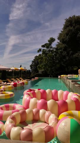 Drone view of a chic villa terrace in Tuscany with bright pools, vintage-style inflatable rings, sun loungers, umbrellas, and a Dolce Vita after-wedding party atmosphere