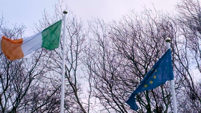 Irish and European Union flags waving in the wind, captured in slow motion under a soft sky