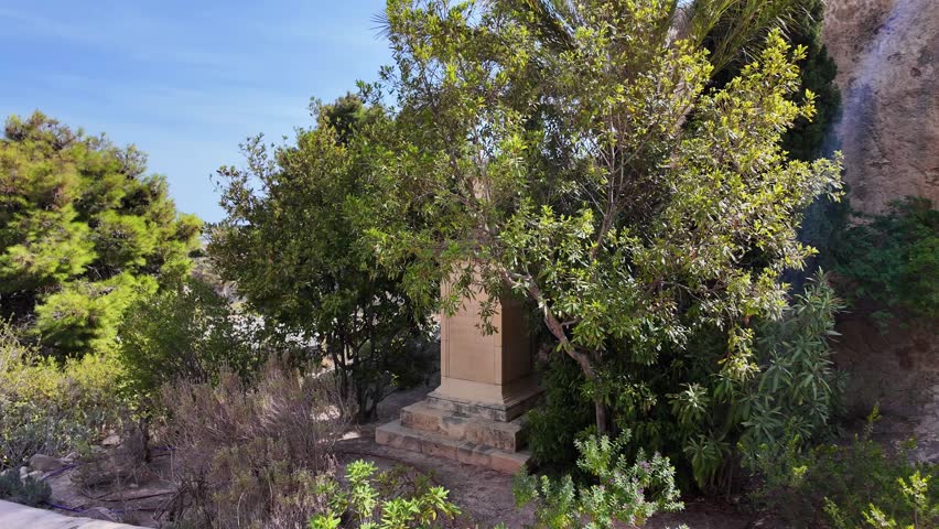 Garden with an urn on a pedestal, surrounded by various plants and tree