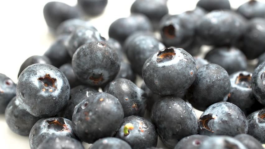 Extreme close-up 4K macro shot of rotating fresh blueberries. Detailed texture of berry skin and stems, filling the frame. Isolated on white background.
