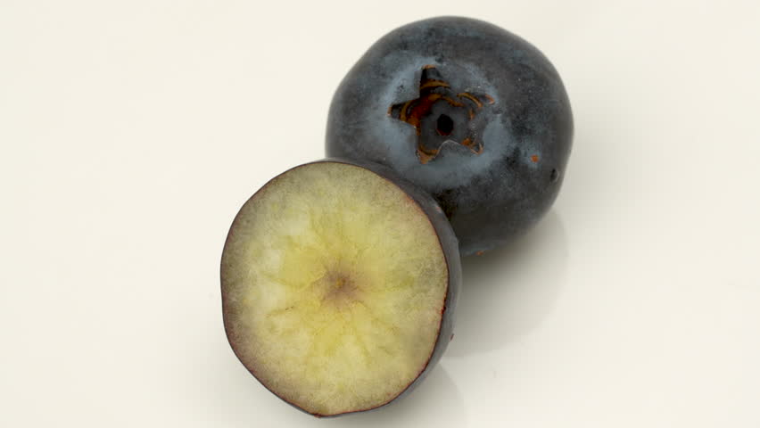 Extreme close-up 4K macro shot of a whole blueberry next to one cut in half, showing the cross-section. Static shot, isolated on solid white background.