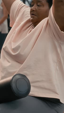 Vertical slowmo shot of concentrated plus size senior Black woman using lat pulldown machine during workout in gym
