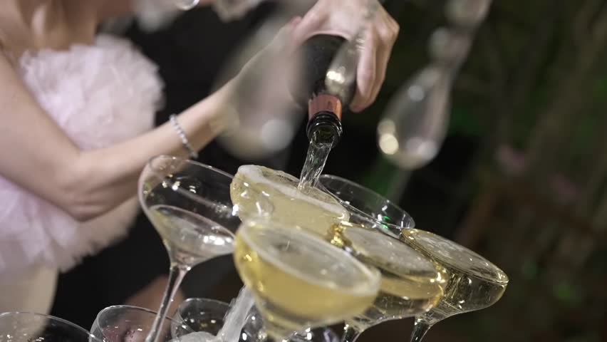 A beautifully lit moment where a couple pours sparkling wine into the top glass of a tiered tower.