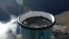 A static close-up shot of hot herbal tea brewing in an enamel mug, featuring tea leaves and lemon slices floating on the surface. Steam rises in the bright, hazy sunlight. - Powered by Shutterstock - Get 15% off with code: PIKWIZARD15