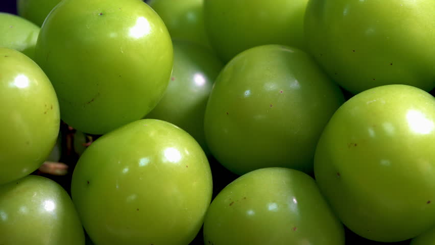 Green grapes rotating.A close-up shows large green grapes rotating on a display stand. They look so delicious. The plumpness of the large grapes is truly enticing.