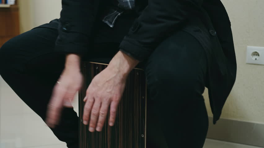 hands beat wooden cajon, percussionist taps box rhythmically, clothing and tone enhance musical