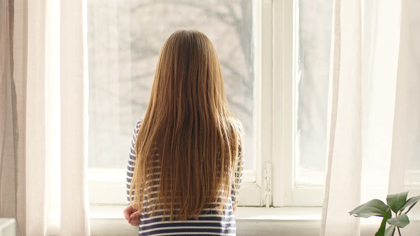 Back view Caucasian little girl child kid looking out window sunny weather shaking long smooth healthy hair turning around smiling going looking at camera walking indoors at home daughter offspring