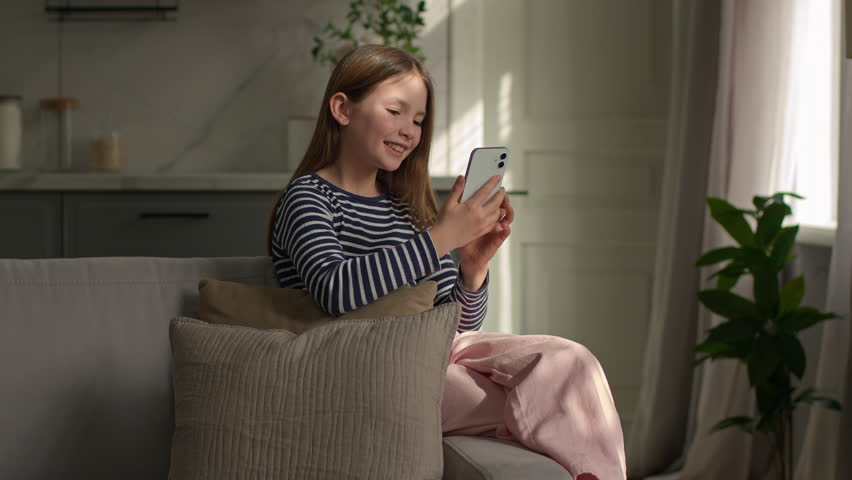 Little Caucasian girl child kid using mobile phone smiling laughing watching funny video gadget addict at home happy daughter chatting scrolling smartphone having fun with internet online social media - Powered by Shutterstock - Get 15% off with code: PIKWIZARD15