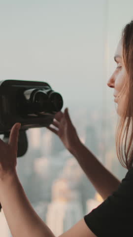 Person looking in binoculars telescope on observation deck for tourist. Tower sky viewpoint top floor. City skyline panorama at day time. Travel, tourism, outdoor lifestyle holiday vacation. Back view