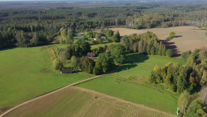 Aerial footage captures vibrant farmland with trees and a pond, highlighting the peaceful landscape as the camera pans, revealing the lush greenery and open fields