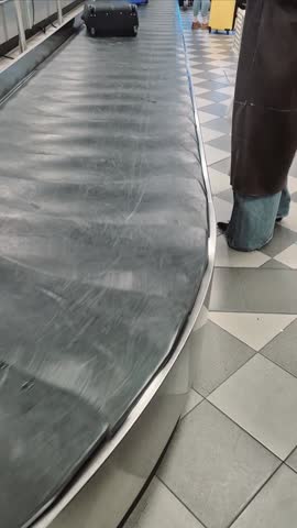 Traveler picks up suitcase from baggage carousel and pulls out the handle to roll it as a trolley in an airport after flight arrival.