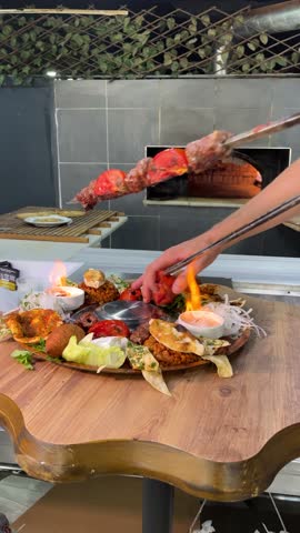Chef serving mixed Turkish kebab platter with flaming presentation, removing meat from skewer over assorted appetizers and grilled vegetables. Authentic Middle Eastern cuisine.