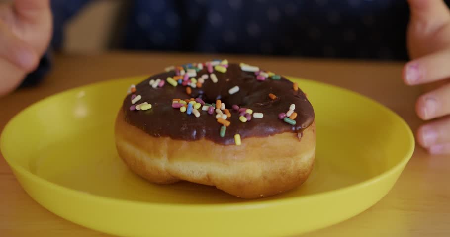 Close-up of a chocolate donut with colorful sprinkles, with a boy in the background