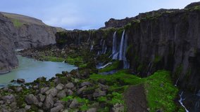 Aerial view shows Sigoldugljufur canyon in Iceland, dark basalt cliffs with multiple slender waterfalls feeding a milky turquoise glacial river, mossy rocks, soft overcast light - Powered by Shutterstock - Get 15% off with code: PIKWIZARD15