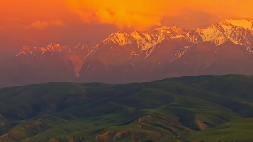 Majestic snow-capped mountains rise above green foothills with in Kyrgyzstan. Drone view with truck to the right camera movement for parallax effect.
