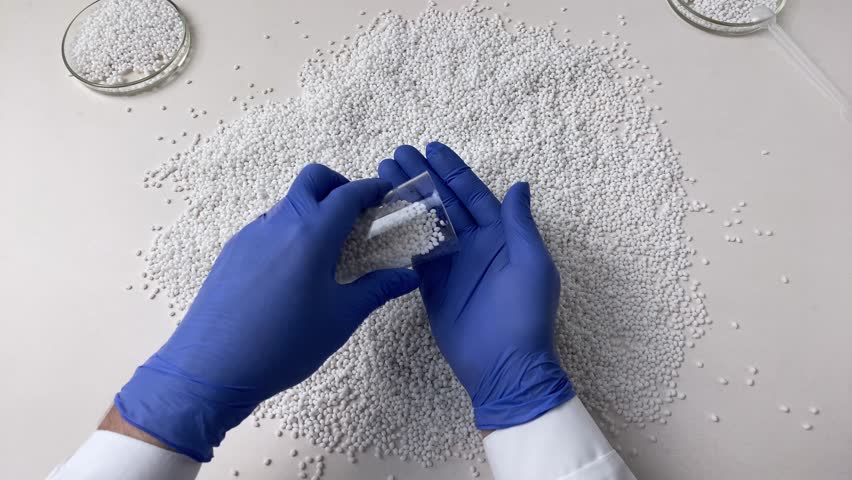 A scientist in a laboratory in blue gloves checks the quality of a batch of white thermoplastic granules. Slow motion.