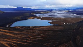 Aerial view shows cobalt lagoon feeding braided meltwater channels across black sand plains, with ochre ridges and volcanic cones under diffuse daylight in Iceland. - Powered by Shutterstock - Get 15% off with code: PIKWIZARD15