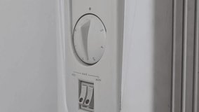 Female hand in a warm green sweater turning the knob of an electric heater to maximum. The heater shows slight signs of wear and dirt - Powered by Shutterstock - Get 15% off with code: PIKWIZARD15