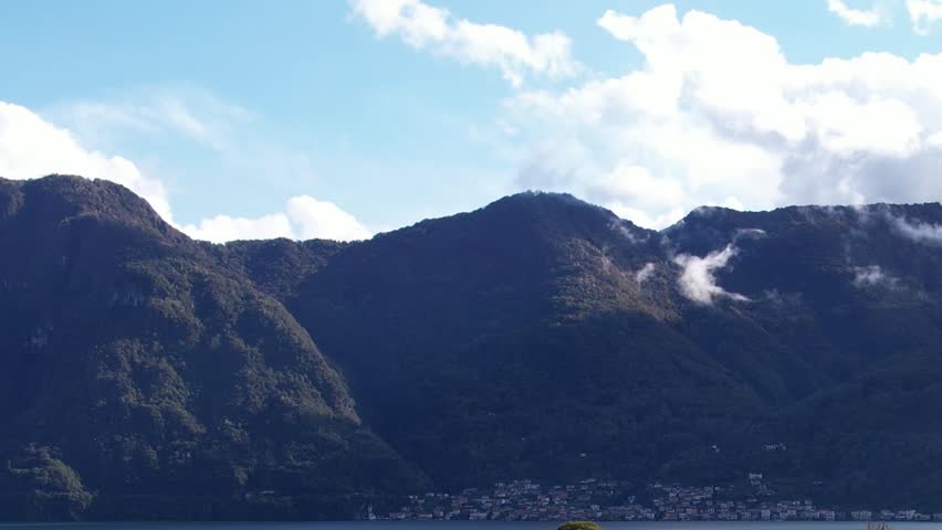 An impressive aerial perspective showcases the majestic Alps in Italy, featuring lush green mountains and a serene sky. Clouds drift lazily over the peaks.