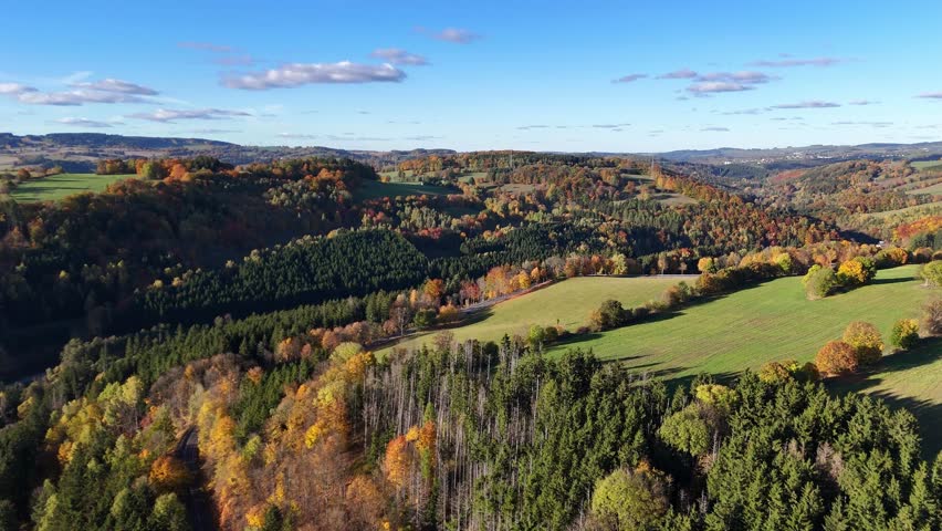 Aerial drone view of autumn forest across mountain slopes, showing layered foliage colors, deep landscape perspective, calm motion, and immersive natural atmosphere in seasonal environment.