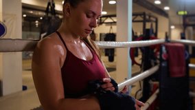 Female boxer leaning against the ropes of a boxing ring wrapping hands with boxing strap. - Powered by Shutterstock - Get 15% off with code: PIKWIZARD15
