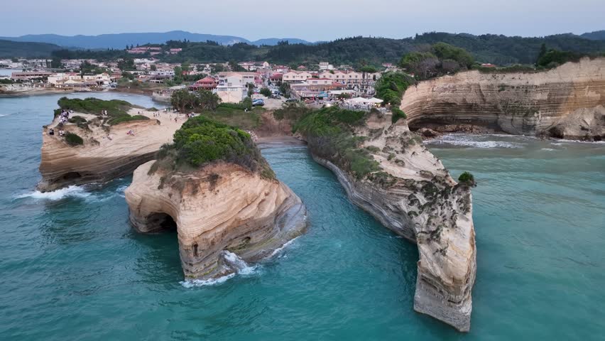 Aerial drone orbit of the iconic Canal d'Amour sea caves and layered cliffs in Sidari, Corfu, revealing the coastal village and Ionian Sea