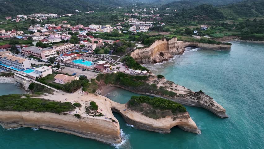 Sweeping high-altitude aerial drone orbit of Sidari, Corfu, Greece, showcasing the famous Canal d'Amour cliffs and the entire coastal town