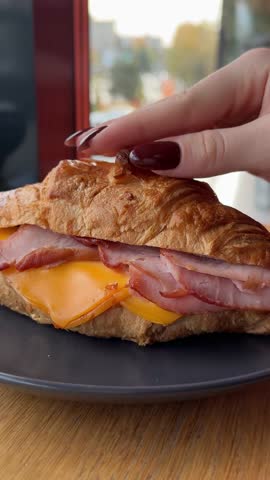 vertical video of a fragrant croissant with cheese and ham standing on a plate and a female hand squeezing it into crumbs useless breakfast pastry cafe restaurant