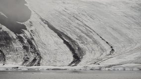 Glacial coastline with dark-streaked snow slopes descending to a frigid sea, scattered ice floes at the waterline, and meltwater channels carving through the pale frozen terrain - Powered by Shutterstock - Get 15% off with code: PIKWIZARD15