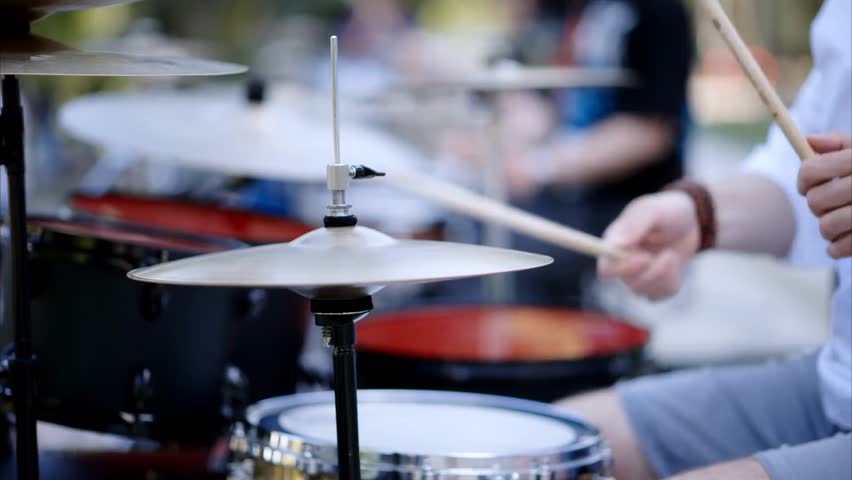Close-up of a man playing red drums outdoors, highlighting musical performance, rhythm, street music, and energetic artistic expression.