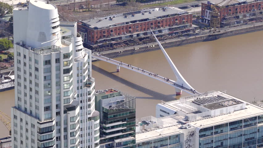 Drone view of Puente de la Mujer bridge over canal with skyscrapers in Buenos Aires